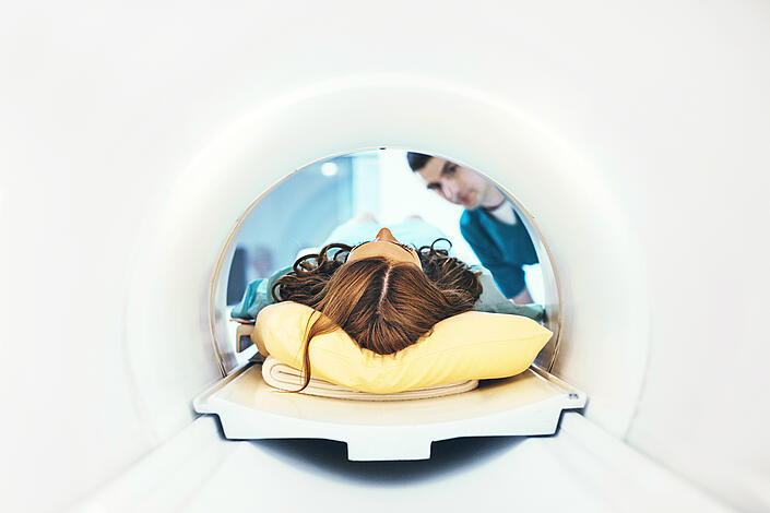Eine Frau wird in ein MRT-Gerät geschoben und ein Pfleger schaut zu.