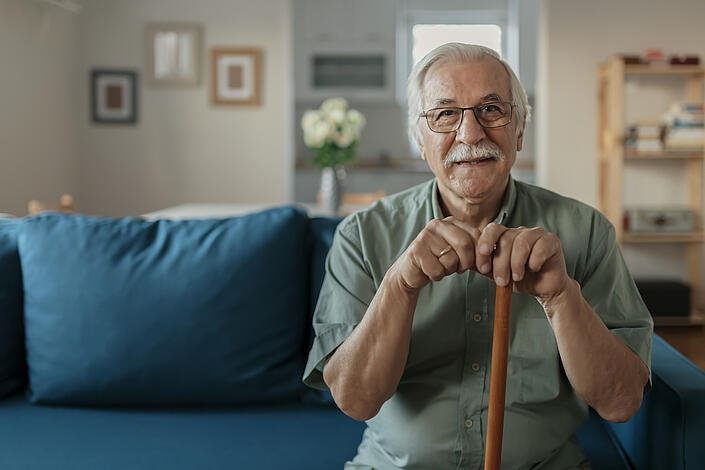 Pflegebedürftiger Senior sitzt zufrieden auf einem Sofa