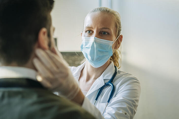 Ärztin mit Maske untersucht Patient
