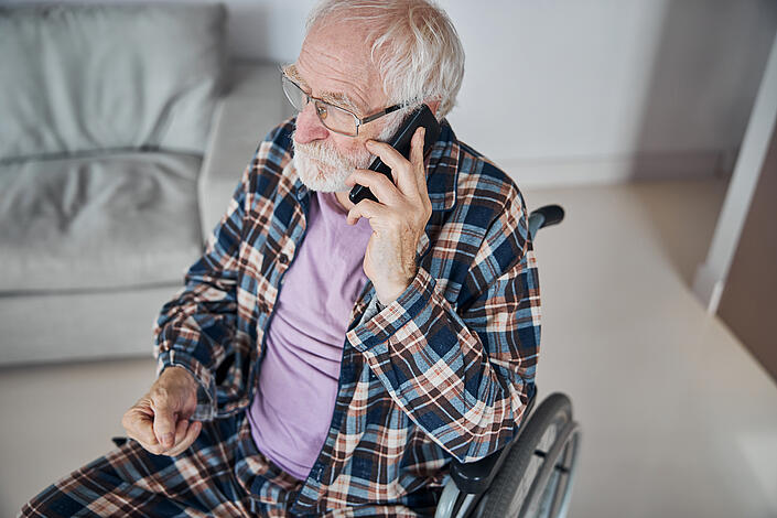 Pflegebedürftiger Senior telefoniert im Rollstuhl