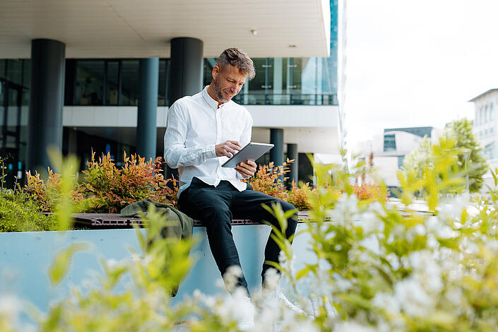 Mann sitzt mit Tablet vor einem Bürogebäude