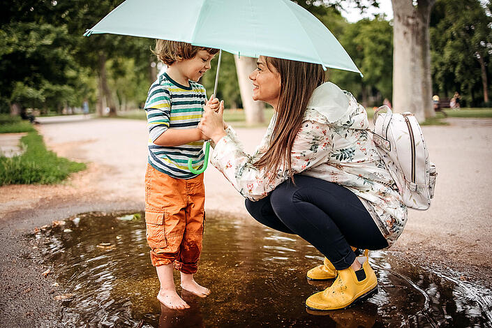 Eine Frau hockt neben einem kleinen Kind unter einem Regenschirm