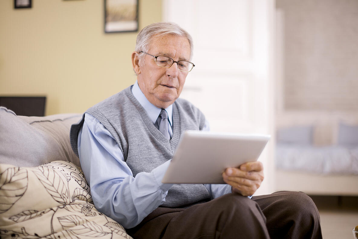 Älterer Herr sitzt mit einem Tablet auf dem Sofa
