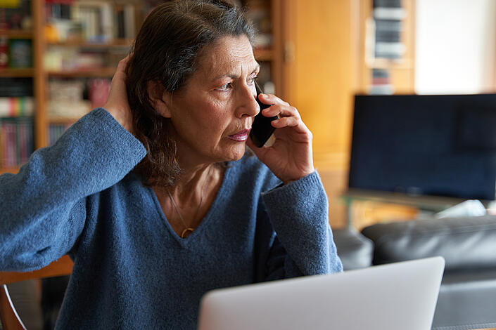 Ältere Frau am Laptop telefoniert konzentriert 